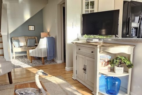 Bright living area with a sectional sofa, white cabinetry, and decorative elements, leading into a cozy nook.