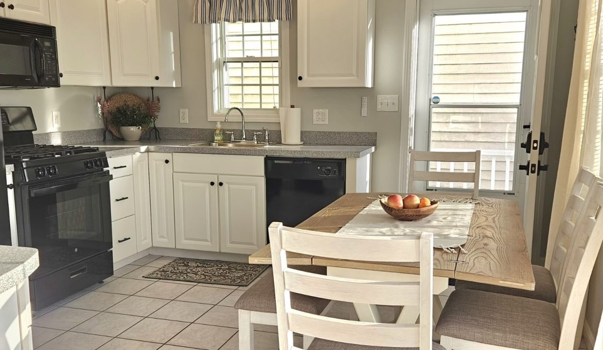 A bright, modern kitchen with white cabinetry and stainless steel appliances, featuring a dining area with a wooden table and chairs.