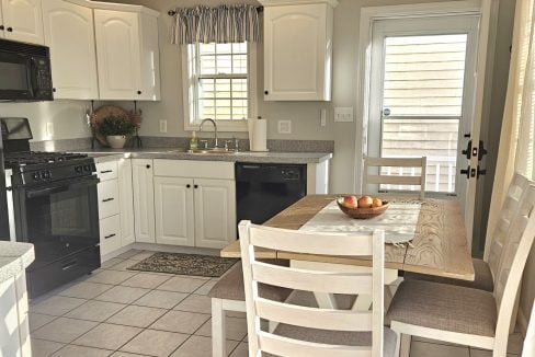 A bright, modern kitchen with white cabinetry and stainless steel appliances, featuring a dining area with a wooden table and chairs.