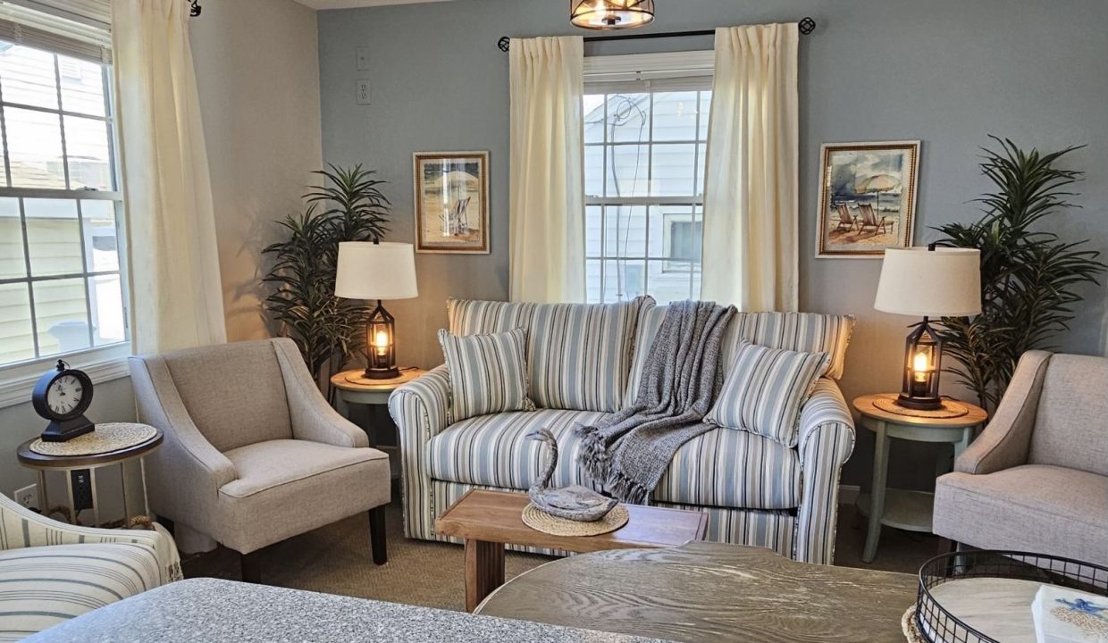 A cozy living room with striped sofa, matching chairs, lamps, and decorative plants.