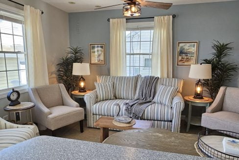 A cozy living room with striped sofa, matching chairs, lamps, and decorative plants.