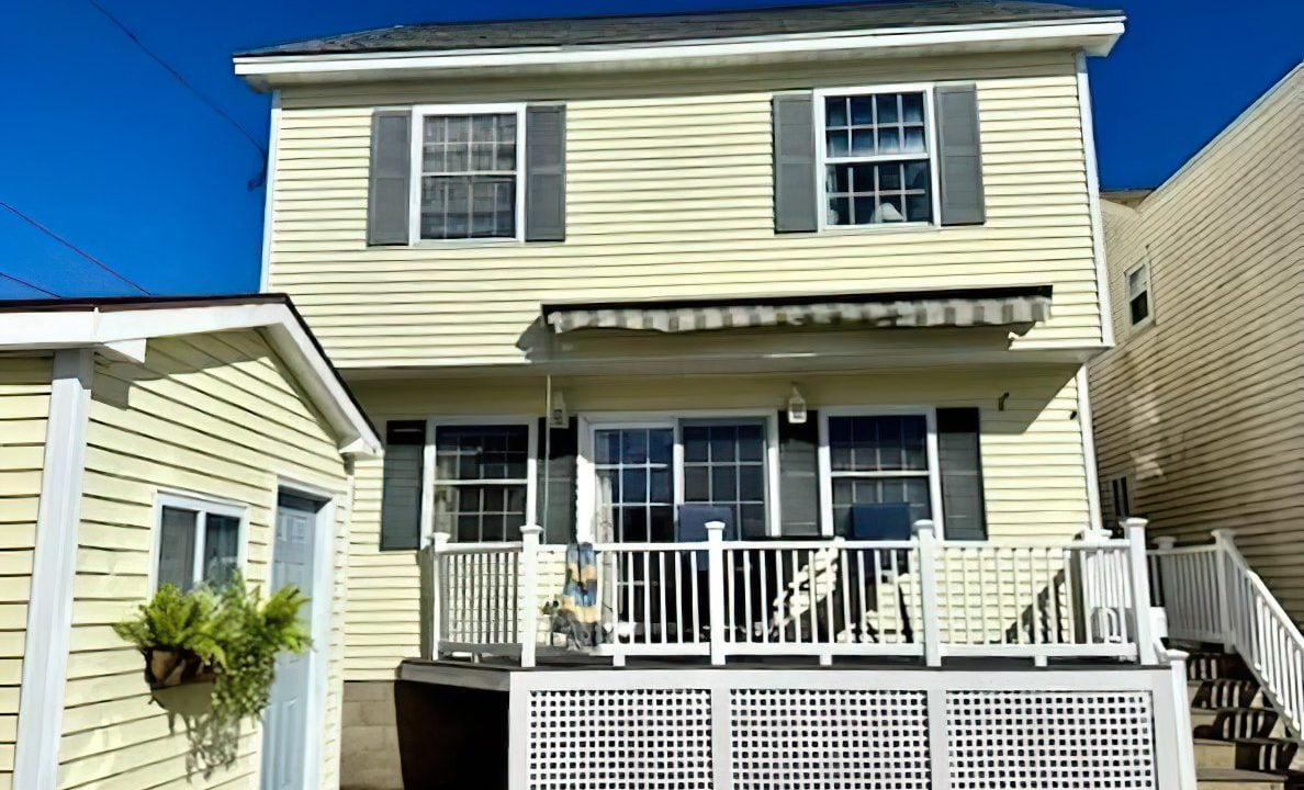 Two-story yellow house with white trim and a front porch under a clear blue sky.