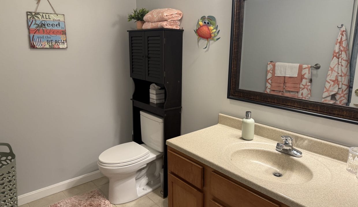 A bathroom with a sink, mirror, toilet, storage cabinet, towel rack, laundry basket, and beach-themed decor.